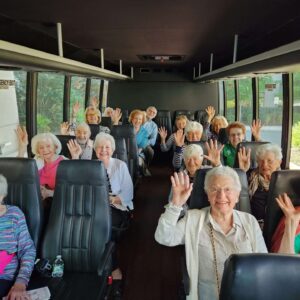 Older adults seated in a bus smiling & waiving at the camera